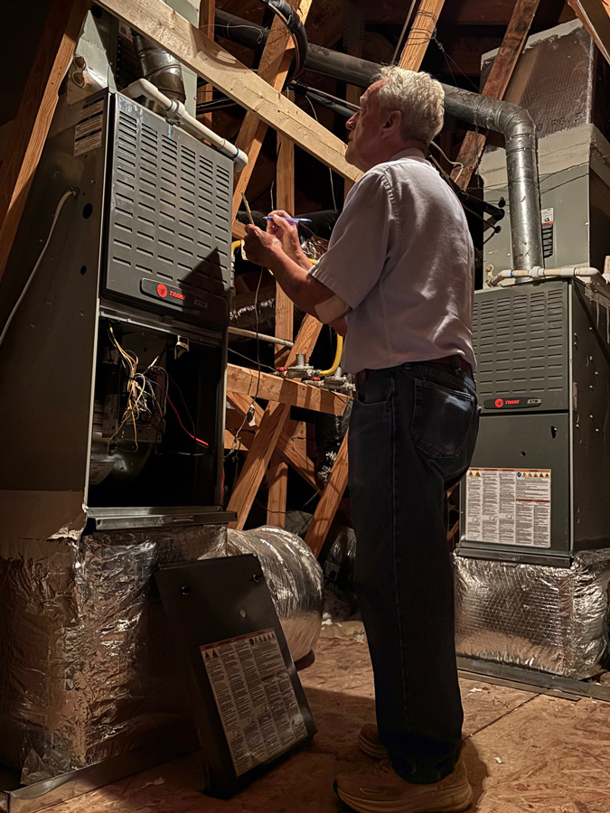 Porter-writing-on-a-pad-in-front-of-ac-air-handler-in-attic